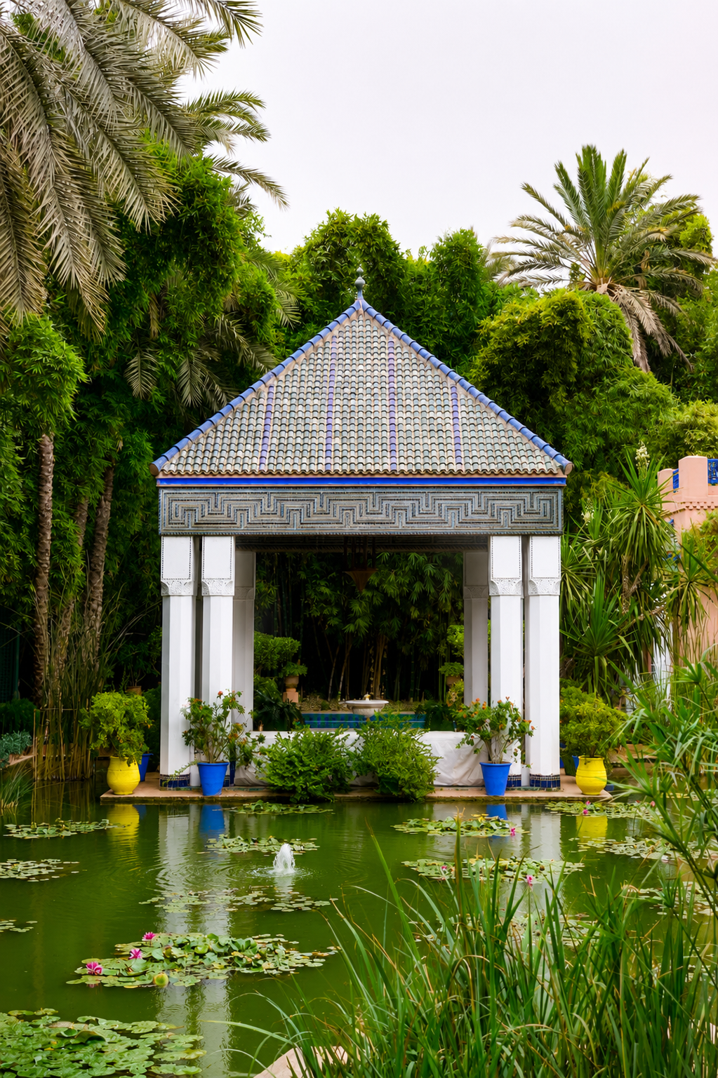 Pavillon traditionnel du Jardin Majorelle à Marrakech entouré de palmiers, d'un bassin avec des nénuphars et d'une végétation luxuriante.