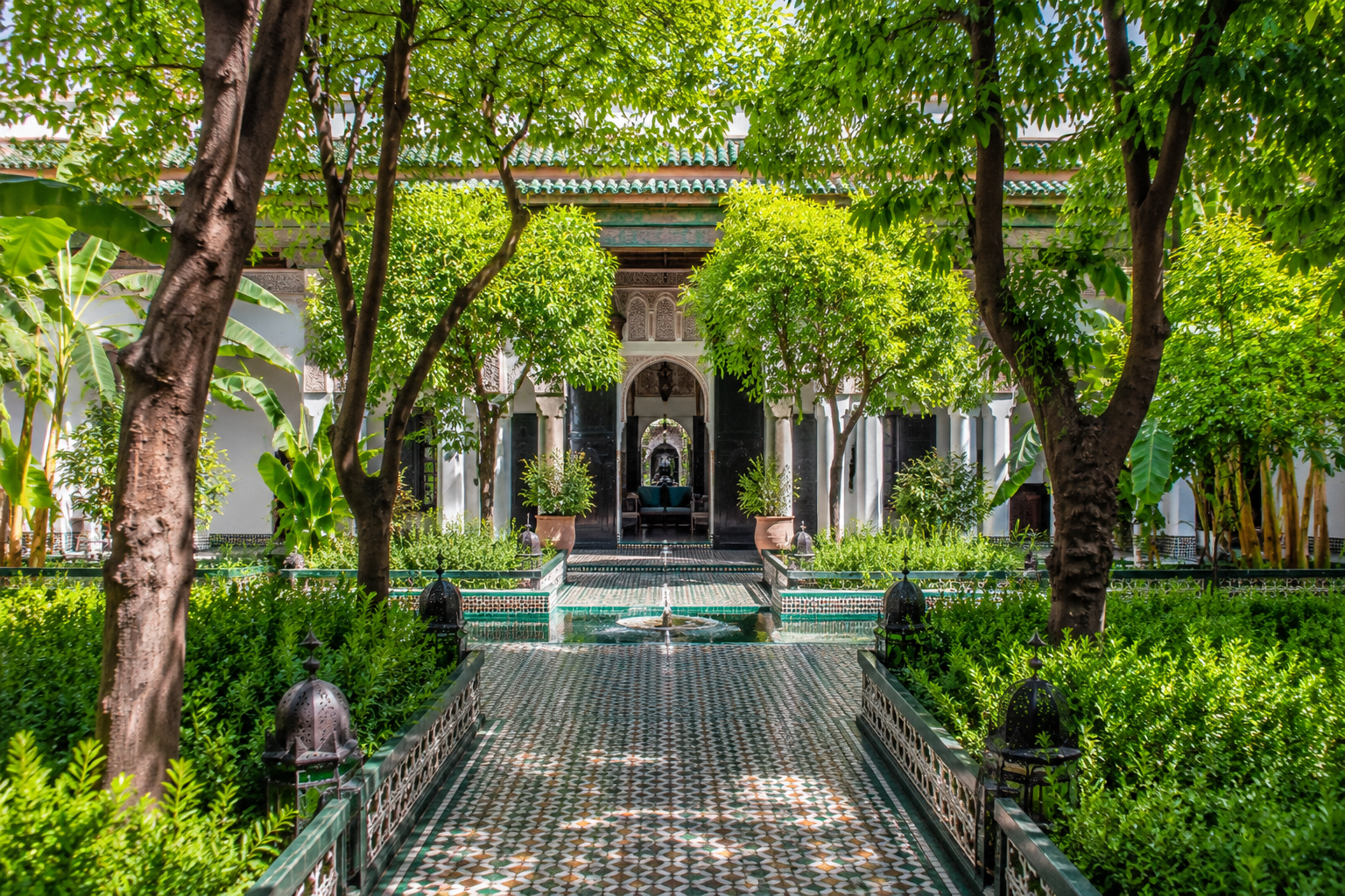 Jardin luxuriant et ombragé à Marrakech avec allées arborées, fontaines et végétation, idéal pour se rafraîchir pendant les fortes chaleurs.